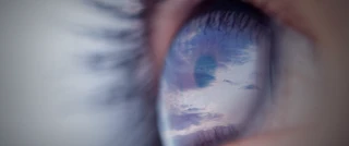 Extreme close-up of an eye reflecting a cloudy sky at sunset, showing detailed eyelashes and the pupil, highlighting the vivid reflection on the cornea.