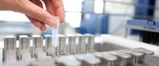Een hand plaatst een klein plastic buisje in een houder van een laboratoriummachine