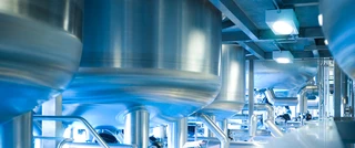 Industrial setting with large stainless steel tanks and pipes in a factory. The bright lighting and blue metallic tones emphasize a clean, efficient atmosphere.