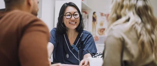 A woman converses with a doctor and two individuals in a medical setting, discussing health-related matters.