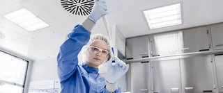 A woman in a lab coat holds a thermometer, looking focused and engaged in her work in a laboratory setting.
