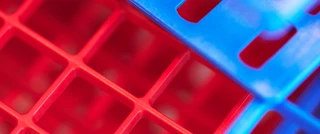 Close-up of interlocking plastic grids in vibrant red and blue colors, creating a geometric pattern. The image conveys a vibrant and modern feel.
