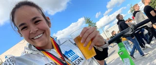 A joyful MJ Rodriguez smiles broadly while holding a beer, after finishing a marathon.