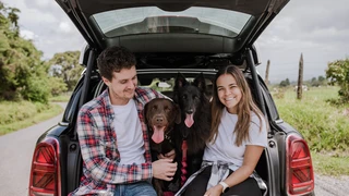 MJ Rodriguez and her partner sit in a car trunk, enjoying time with their two dogs in a relaxed outdoor setting.