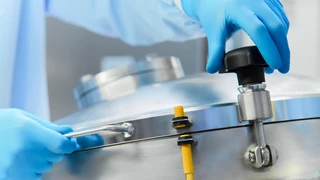A person wearing blue gloves is carefully holding a shiny metal object in their hands.