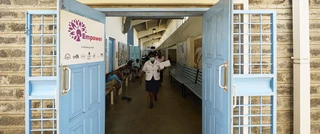 A woman is seen walking through a bold blue door, the entrance of a cancer care clinic.