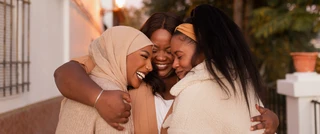 Three women embrace each other joyfully, sharing smiles in a warm and friendly atmosphere.
