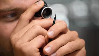 A man uses a magnifying glass to inspect a pointy object