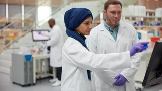 Two scientists in white lab coats working on lab analyzers in Building E.