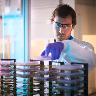 A man wearing a lab coat is engaged in operating a machine, demonstrating a scientific process in a lab environment.