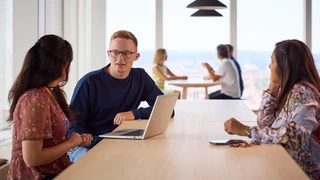 Three colleagues in discussion at a work bench.