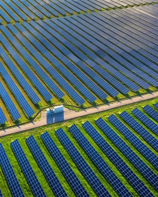 Aerial view of a solar farm surrounded by a vast green field under a clear blue sky.
