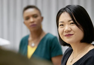 A woman in a green shirt sits in front of a group of people, engaged in conversation or discussion.